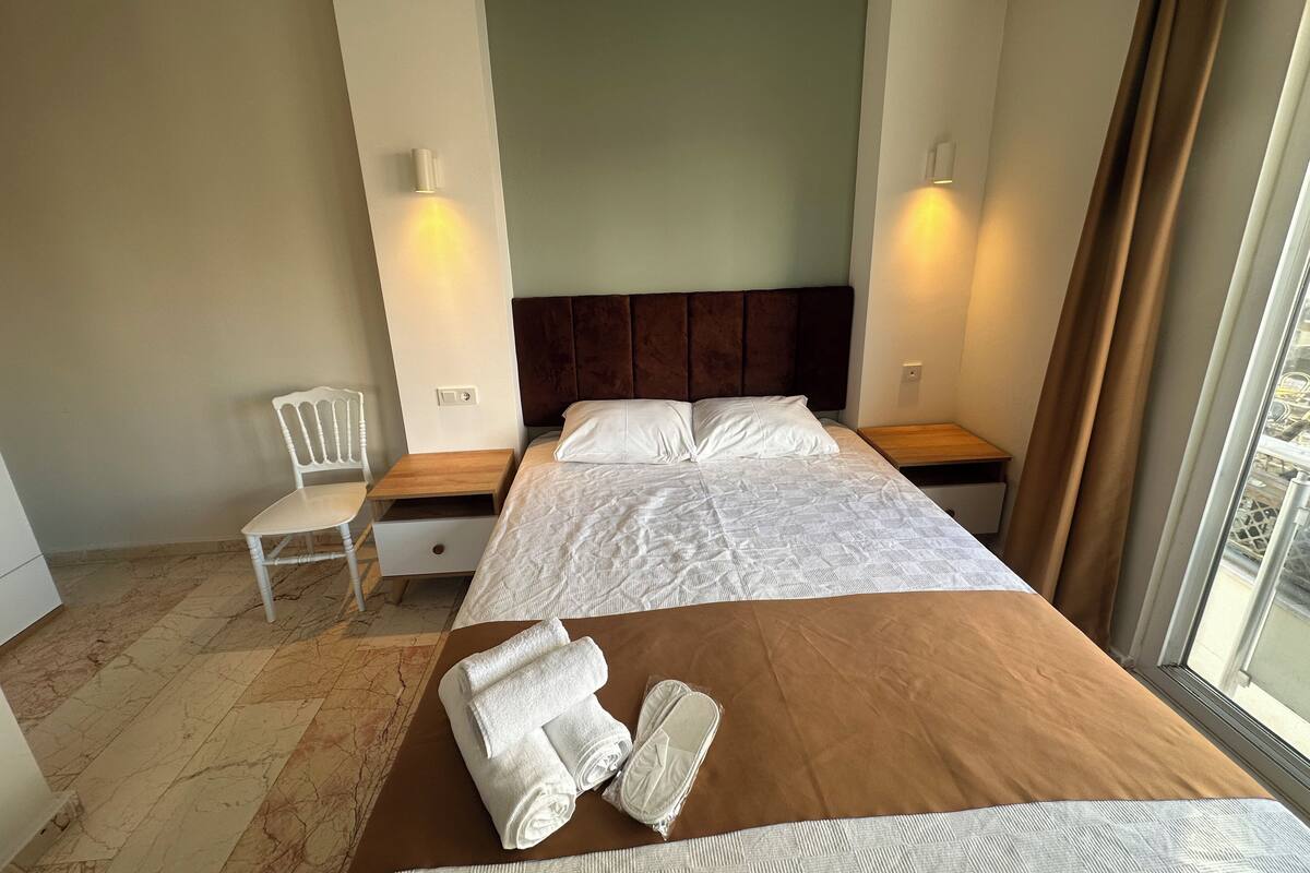 A hotel room with a large bed, a nightstand, a chair, and a window with curtains.