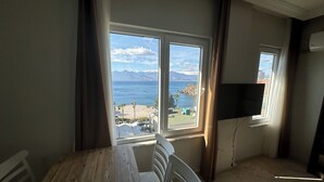Ein Zimmer mit einem Holzespeisetisch und Stühlen, einem an der Wand befestigten Fernseher und einem großen Fenster mit Blick auf das Meer und die Berge.