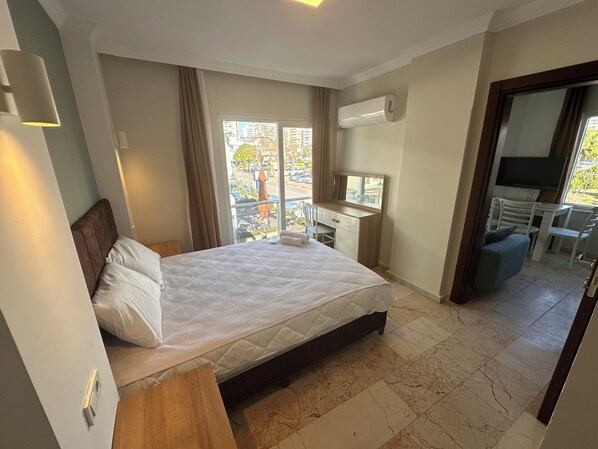 A hotel room with a bed, a desk with a mirror, a TV, and a balcony with a view of the city. - Dagtekin Apartments (Antalya)