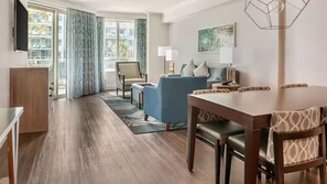 A modern hotel room with a dining area, a sofa, a lamp, and a view of the outdoors. - Perfect Family Friendly Beach Stay-Ocean Oak Resort by Hilton-2 Bd. Oceanfront (Hilton Head Island)