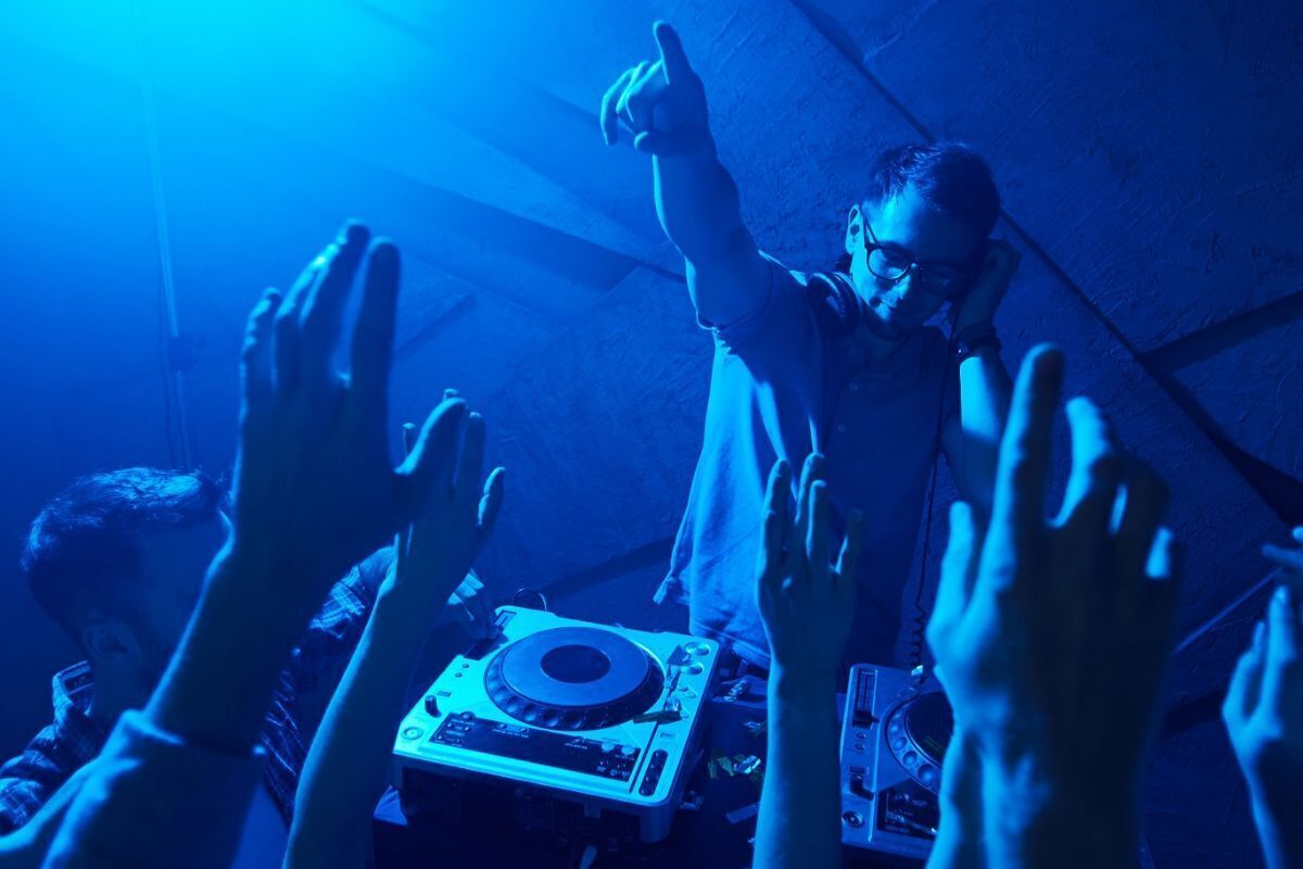 Ein DJ tritt in einem schummrigen Raum auf, das Publikum streckt die Hände hoch.