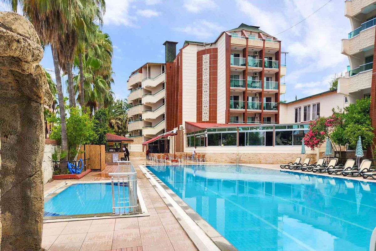 Un hotel con piscina, varios balcones y vistas a palmeras.