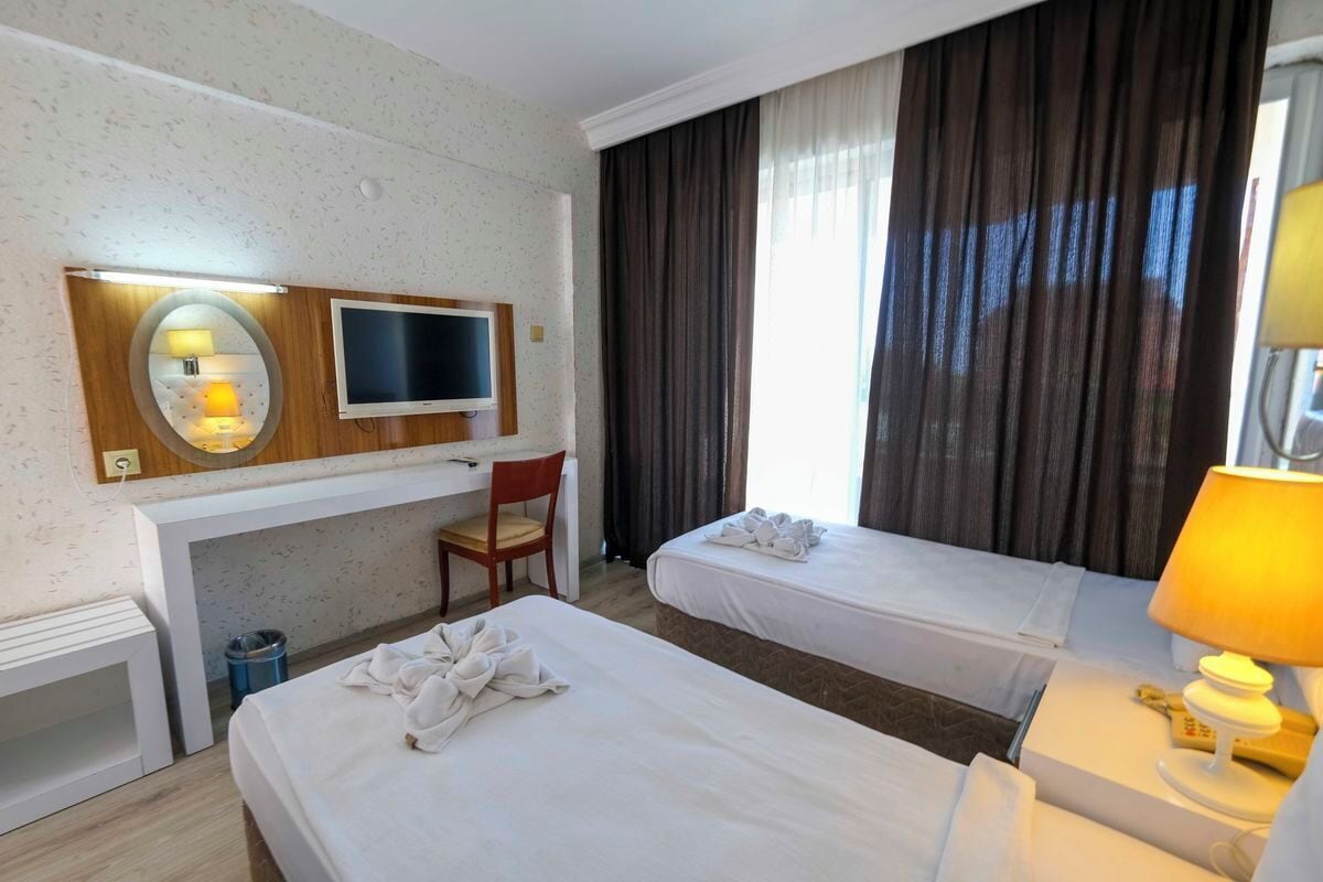 Quarto de hotel com duas camas, uma escrivaninha, televisão, uma cadeira e uma luminária.