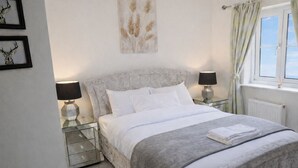 Un lit bien fait, avec du linge de lit blanc, deux lampes de chevet, une tête de lit en marbre et une fenêtre avec des rideaux.