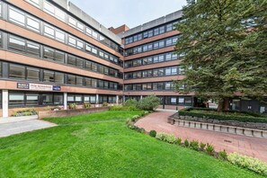 A modern building with multiple floors, large windows, and a well-maintained courtyard with grass and pathways.