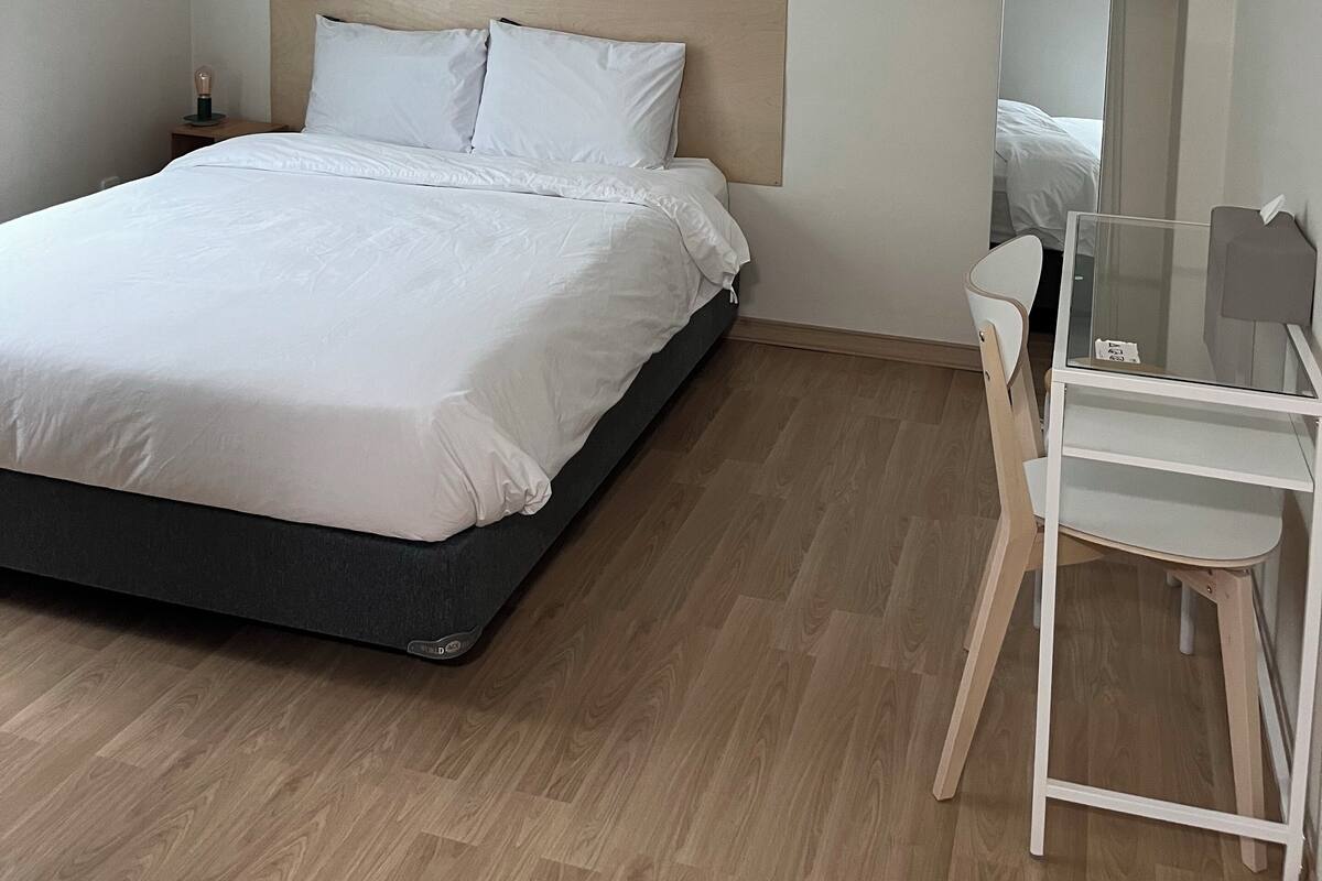 Un dormitorio moderno con cama, mesita de noche, silla y espejo.