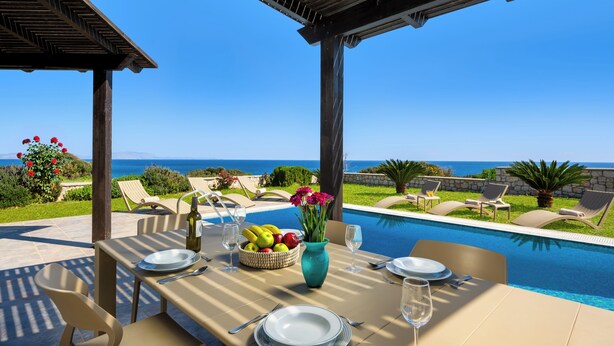 A poolside dining area with a table set for two, a vase of flowers, and a bowl of fruit. - Aqua Natura Villas - Villa Aqua (Rhodes)