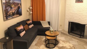 Una sala de estar con un sofá seccional, una mesita redonda, una chimenea y un cuadro en la pared.