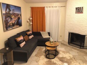 Ein Wohnzimmer mit Ecksofa, einem kleinen runden Tisch, einem Kamin und einem Bild an der Wand.