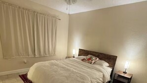 Un dormitorio con una cama, dos mesitas de noche con lámparas, un ventilador de techo y una alfombra estampada.