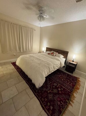 Ein Schlafzimmer mit einem Bett, zwei Nachttischen mit Lampen, einem Deckenventilator und einem gemusterten Teppich.