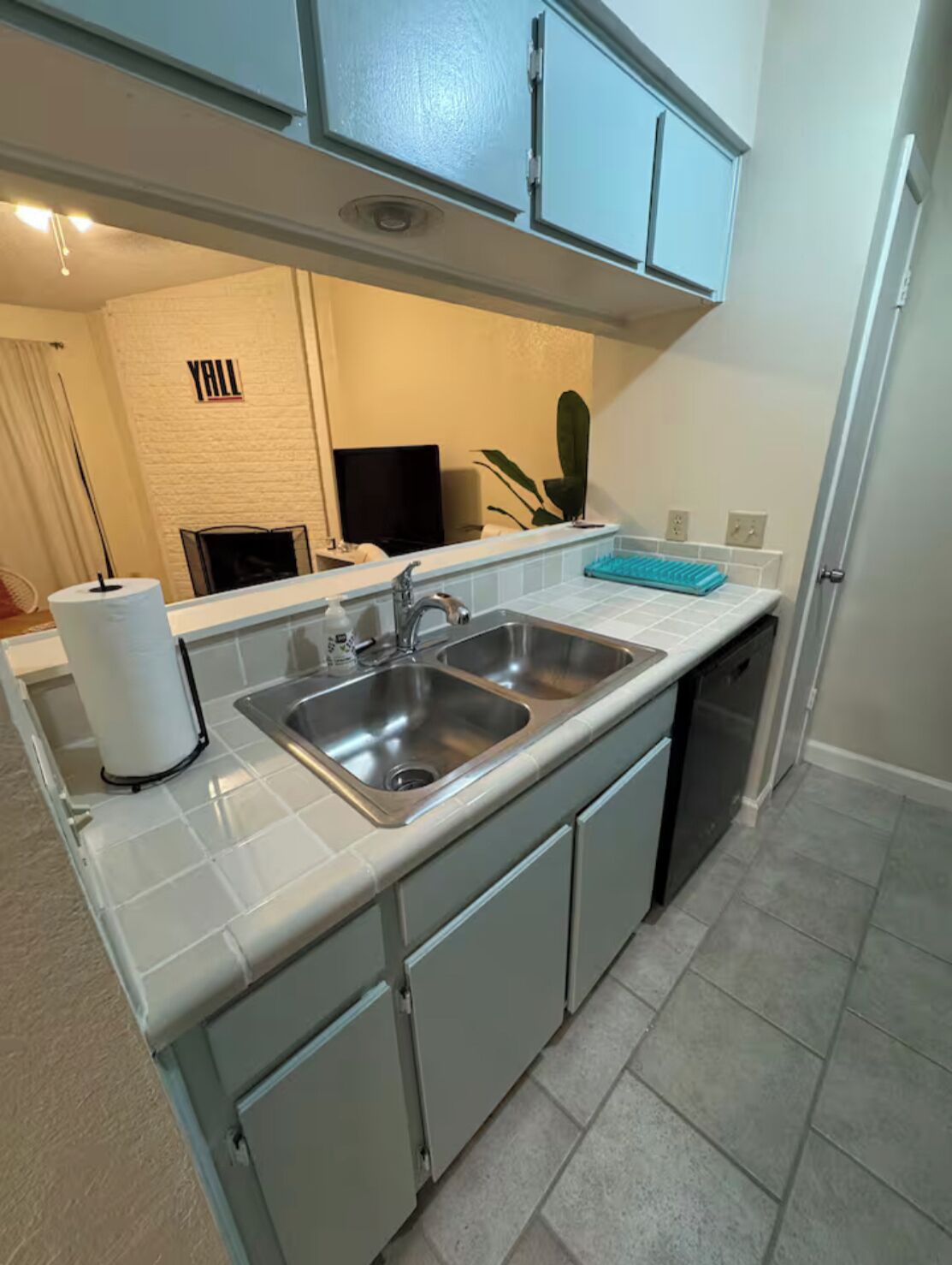 Cocina compacta con un lavaplatos doble, un escurreplatos y un televisor de pantalla plana al fondo.