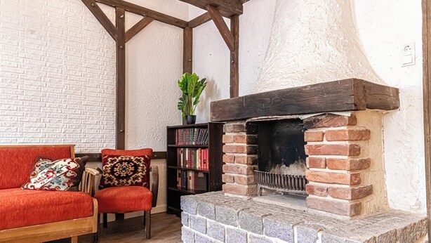 A cozy room with a brick fireplace, a red sofa, a wooden chair, and a bookshelf filled with books. - Vintage 2BR U6 Schoepfwerk Long Stay (Vienna)