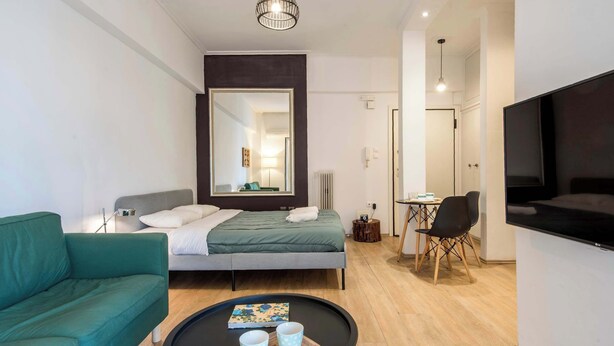 Una habitación de hotel moderna con una cama, un sofá verde, una pequeña mesa de comedor con sillas, un televisor y un espejo grande.