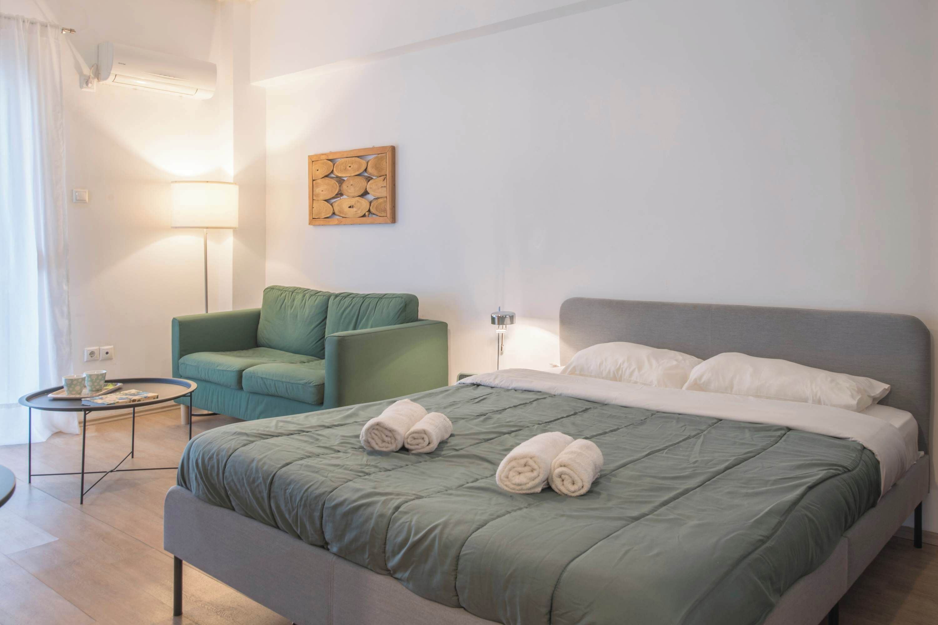 Une chambre d’hôtel bien aménagée, avec un lit, un canapé vert, une petite table et une œuvre d’art accrochée au mur.