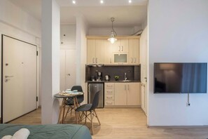 A compact hotel room with a bed, a small dining table with chairs, a kitchenette with a microwave, and a TV mounted on the wall. - City Nest  in the center of Athens (Athina)