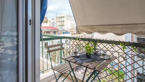 Un balcón con una mesa, sillas, una planta en maceta y vistas a edificios y vegetación.