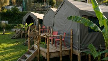Twee tenten met een houten terras en rode stoelen, omringd door groen.