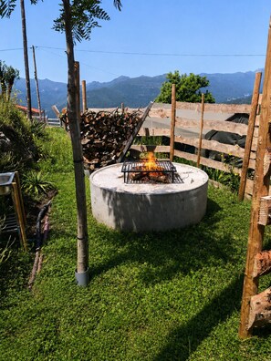Un foyer en bĂ©ton, entourĂ© dâune clĂŽture en bois, avec une pelouse et une vue sur les montagnes en arriĂšre-plan.