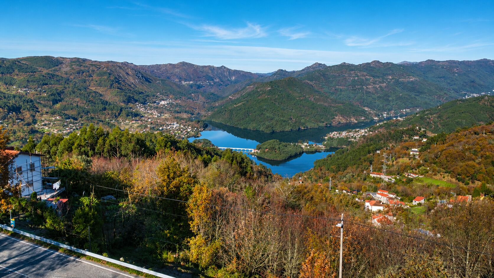 Paisatge de muntanyes amb un llac, cases i una carretera.
