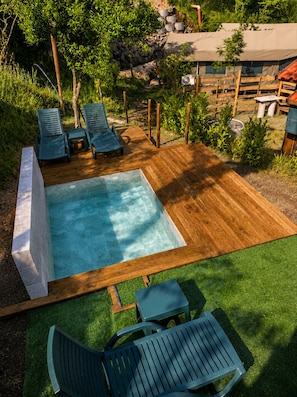 A wooden deck with a swimming pool, lounge chairs, and a small table.