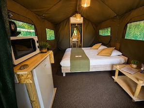 A tented room with a bed, a microwave, a small fridge, and a table with a plant.