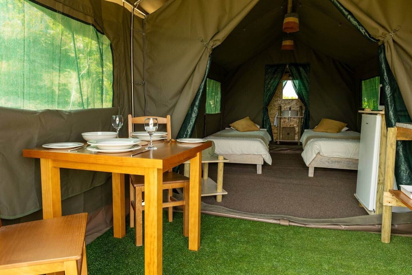 Acomodação em tenda com mesa de jantar, duas camas e uma pequena cozinha.