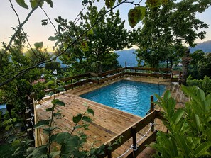 Une piscine rectangulaire dotĂ©e dâune terrasse en bois et entourĂ©e dâune clĂŽture en bois, le tout nichĂ© au cĆur dâune vĂ©gĂ©tation luxuriante et offrant une vue imprenable sur un paysage montagneux.