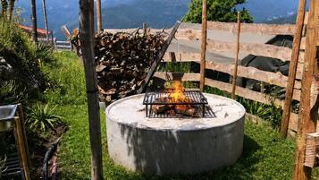 Ein Beton-Feuerkorb, umgeben von einem Holzzaun, mit einer Rasenfläche und einer Bergblick im Hintergrund.