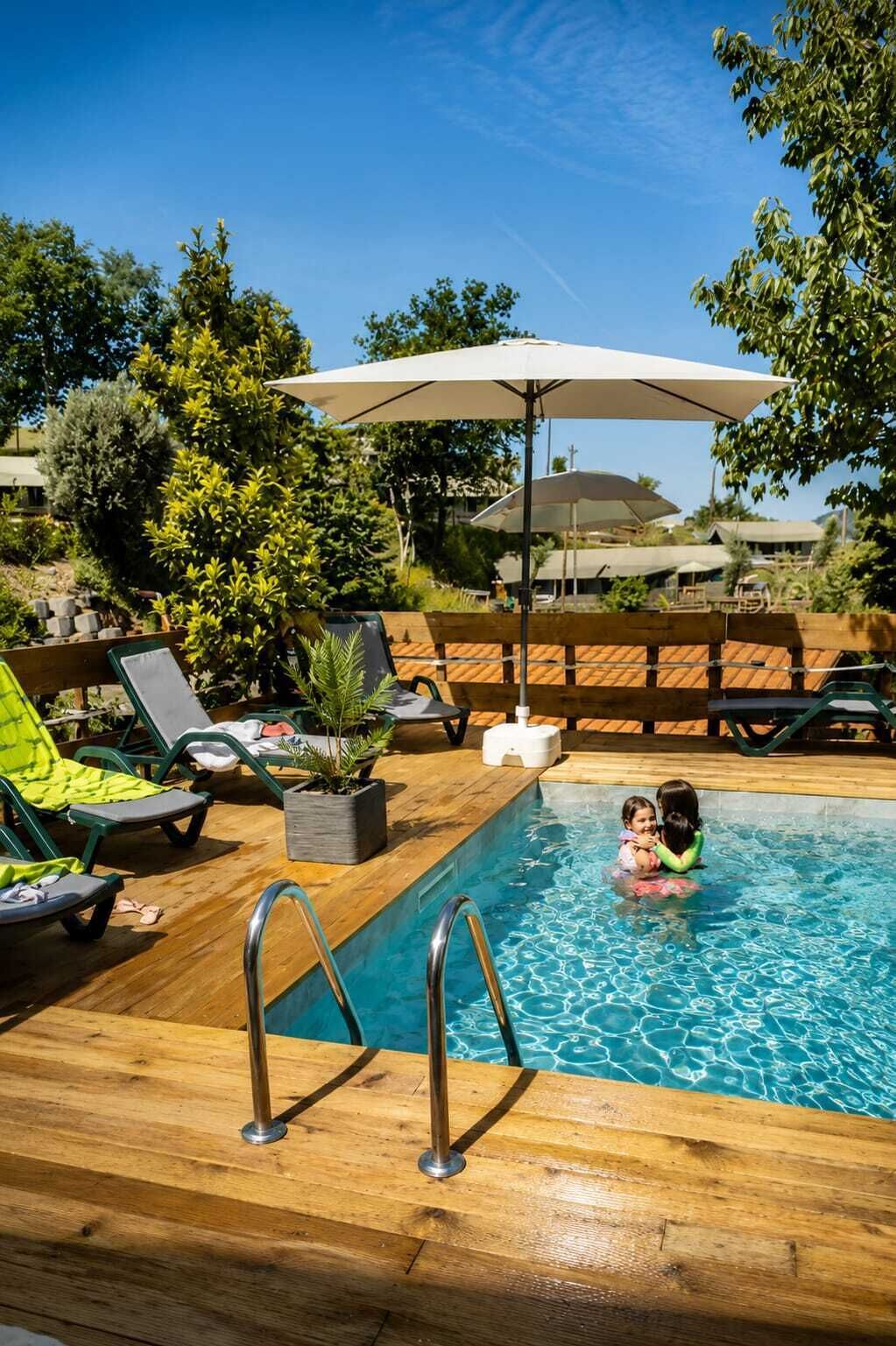 Un espace aménagé au bord de la piscine, avec des chaises longues, une terrasse en bois et une petite piscine.