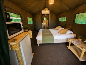 Ein Zeltezimmer mit Bett, einer Mikrowelle, einem kleinen Kühlschrank und einem Tisch mit einer Pflanze.