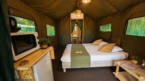 Habitación con carpa, una cama, microondas, refrigerador pequeño y una mesa con una planta.