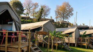 Un camping con varias tiendas de campaña, una terraza de madera y un cartel que indica 'CAMPAS'.