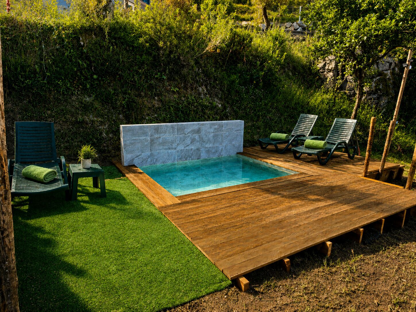 Ein rechteckiger Pool mit einer gefliesten Wand, umgeben von Holzdeck und künstlichem Rasen.