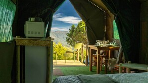 A tented accommodation with a bed, a table set for dining, and a view of the outdoors.