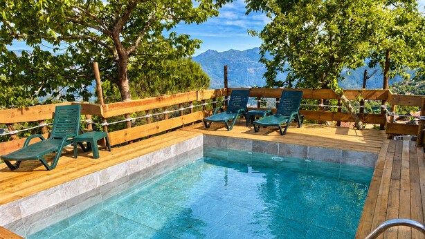 A pool area with wooden deck, green lounge chairs, and a view of mountains.