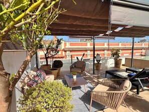 Eine Dachterrasse mit Gartenmöbeln, einem Blumentopf und Blick auf Gebäude im Hintergrund.