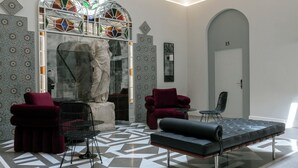 A modern lobby with geometric patterned flooring, a seating area with red and black furniture, and a large stained glass window. - Hotel Boutique Casa Romana Villa (Seville)