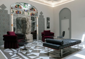 Un vestíbulo moderno con suelo de estampado geométrico, un área de descanso con muebles rojo y negro, y un gran ventanal de vitral.