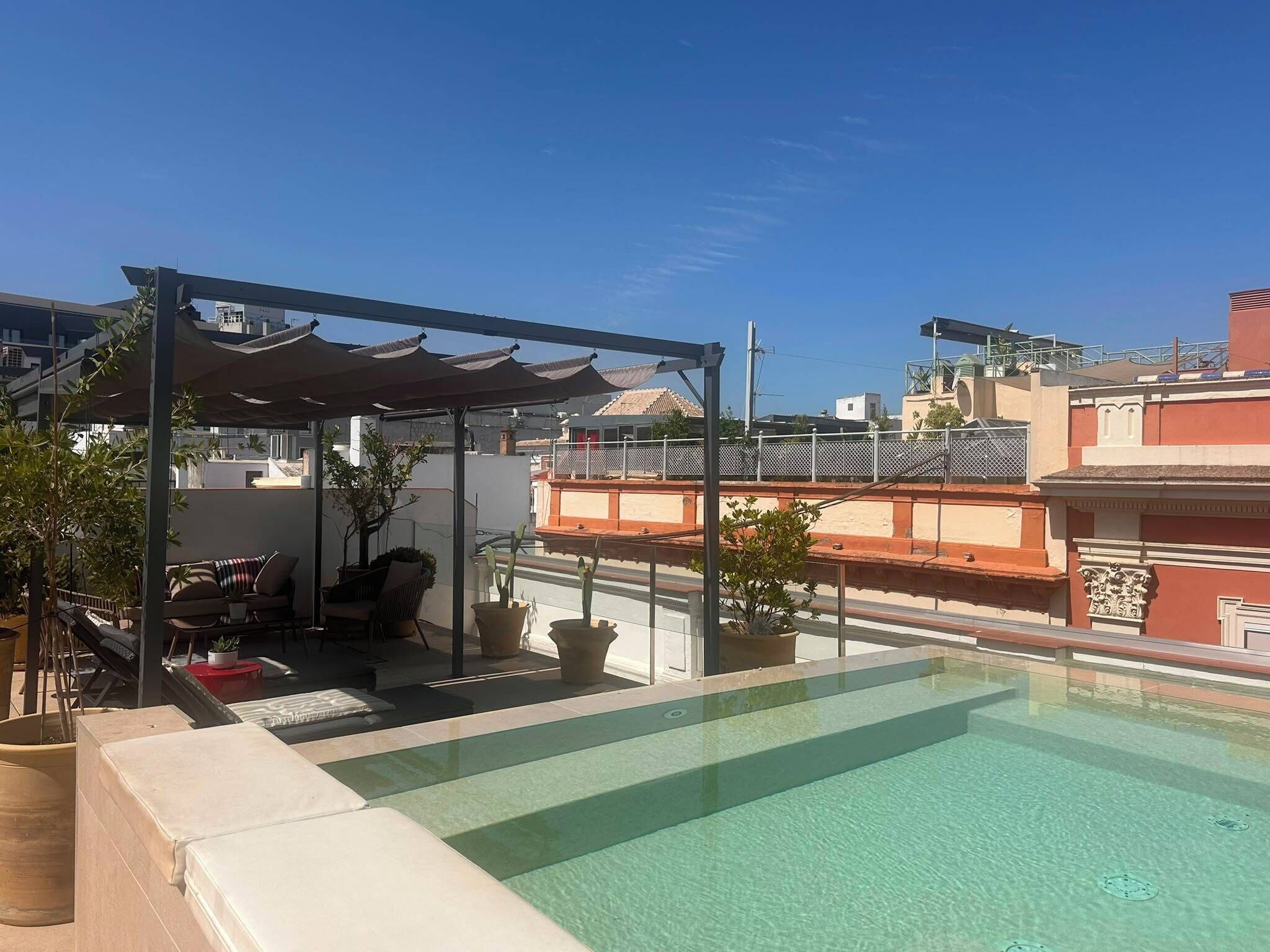 A rooftop pool with a covered seating area and potted plants.