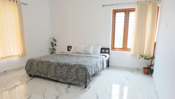 A spacious bedroom with a large bed, a ceiling fan, and a potted plant. - near beach 8 rooms  place where peace, quiet & calmness meet (Varkala)