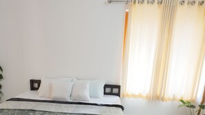 A bedroom with a bed, a nightstand, a potted plant, and a window with curtains. - near beach 8 rooms  place where peace, quiet & calmness meet (Varkala)