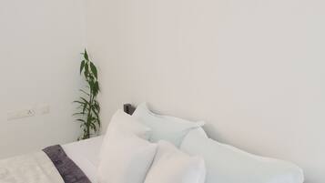 A neatly made bed with white and light blue pillows, a dark blue and white patterned bedspread, and a green plant beside the bed.