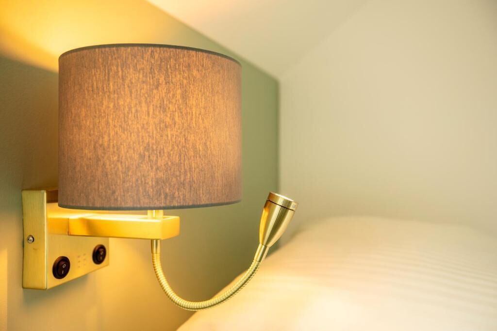 A wall-mounted lamp with a cylindrical shade and a flexible neck, attached to a brass fixture.