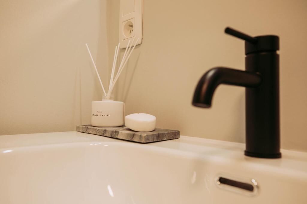 A bathroom sink with a black faucet, a white soap dish, and reed diffusers.