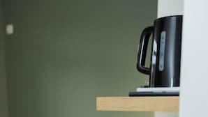 A kitchenette with a coffee maker, a stack of plates, and a grey sofa in the background.