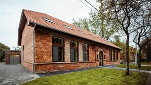 A brick building with a red-tiled roof, large windows, and a grassy lawn.