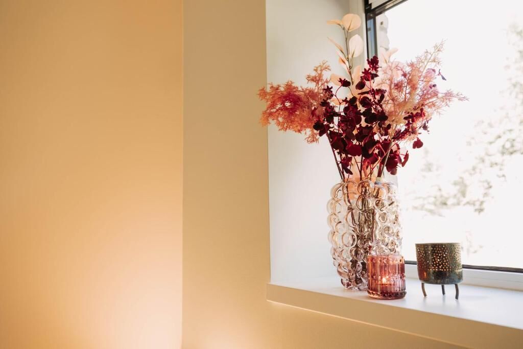 A vase with flowers on a windowsill next to a candle.