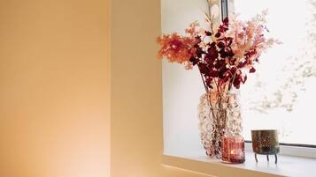 A vase with flowers on a windowsill next to a candle.