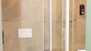 A bathroom with a toilet, a trash bin, and a glass-enclosed shower area.
